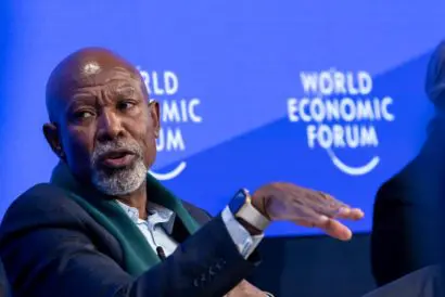 Lesetja Kganyago speaking and gesticulating with one hand, in front of a blue backdrop embloazioned with the World Economic Forum logo