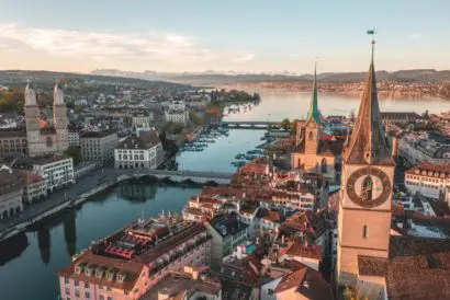 An elevated view of Zurich with Lake Zurich in the background. Dawn sunlight colours the buildings