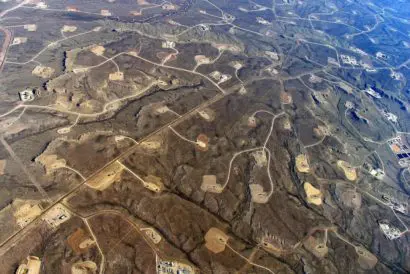 An aerial shot of an open landscape, dotted with fracking installations and roads between them