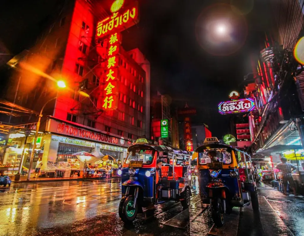 A street at night, illuminated by neon signs in Chinese and Thai script.