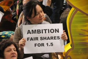 a woman holds a sign that reads: ambition, fair shares for 1.5